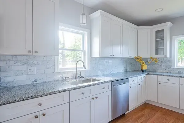 A kitchen with white cabinets , granite counter tops , a sink , and a window.