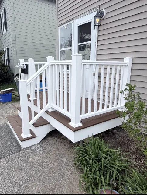 Small white wooden accessibility ramp with railings beside a beige house entrance