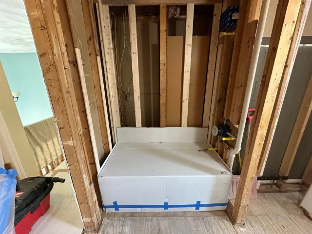 Construction site: A white bathtub base is installed between wooden studs.