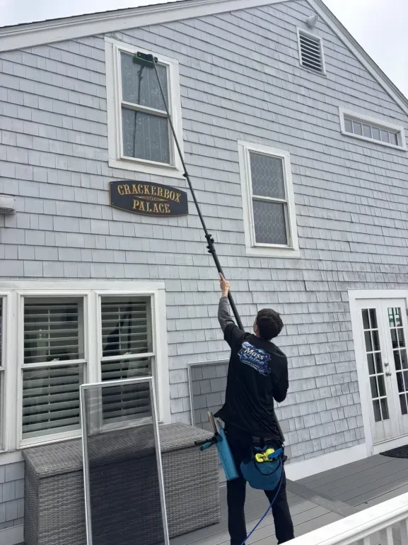 Mass Shine crew member using extension pole to clean second story window on shingle home South Shore MA