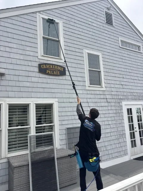 Mass Shine crew member using extension pole to clean second story window on shingle home South Shore MA
