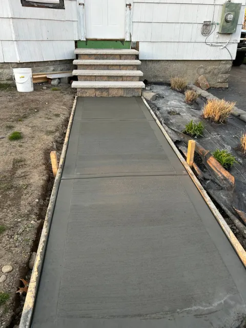 Concrete walkway leading to mobile home entrance with stone steps and wooden border edging