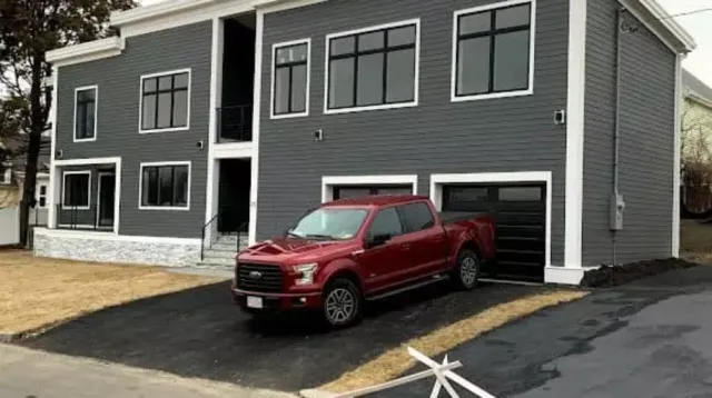 Modern gray multi-family home with black windows, garage bays, and driveway, located in the Greater Boston area