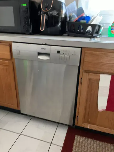 Kitchen with a stainless steel dishwasher between wood cabinets under a countertop with appliances.