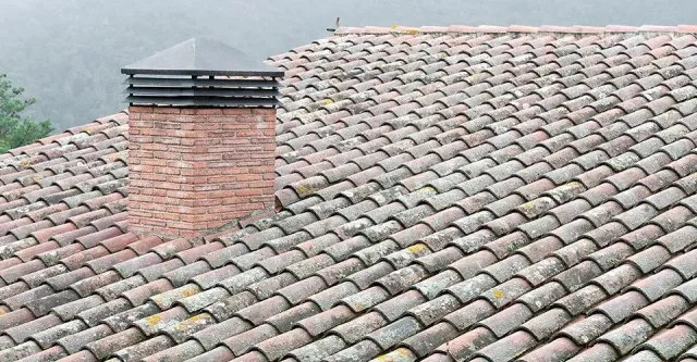 A brick chimney on top of a tiled roof.