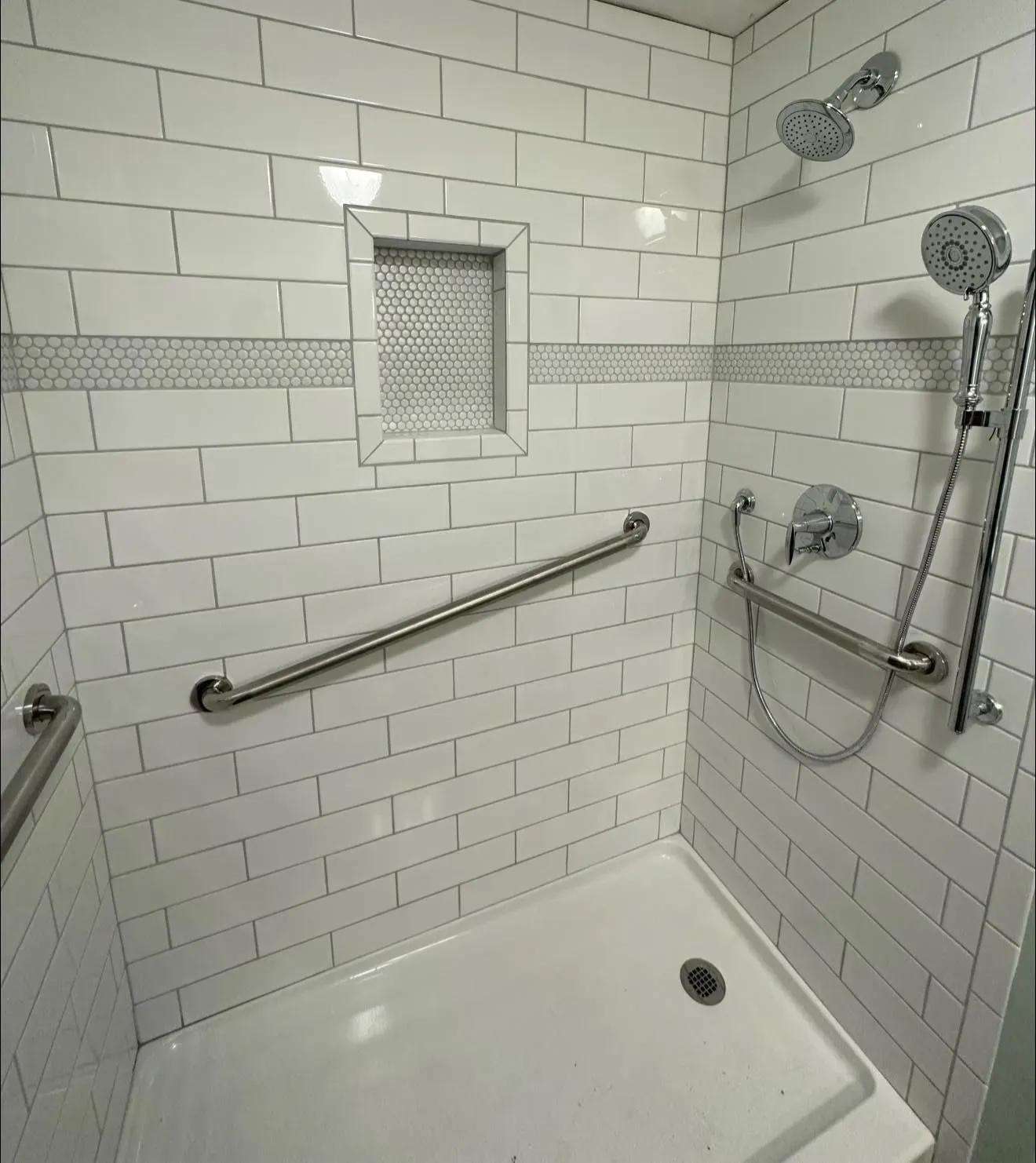 A bathroom with white brick walls and a walk in shower with a hand rail.