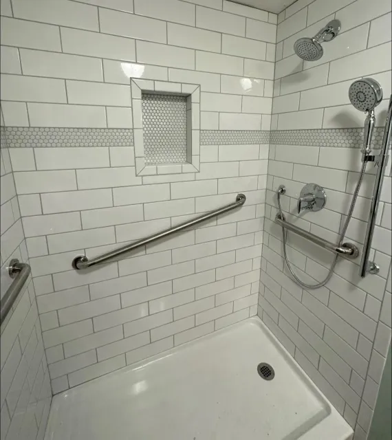 A bathroom with white brick walls and a walk in shower with a hand rail.