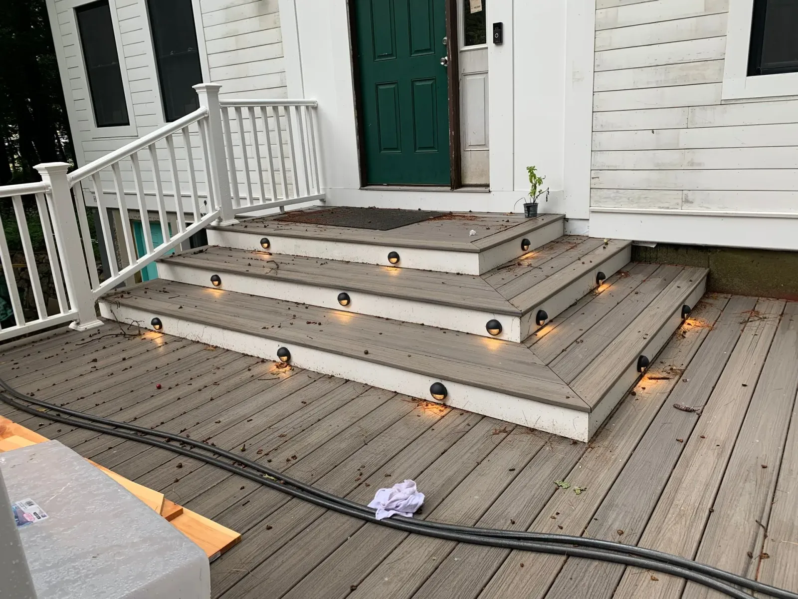 Wooden steps with lights leading to a green door of a white house.