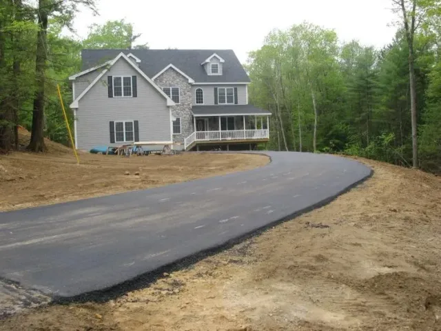 Two-story house with a long, curved asphalt driveway and a wooded backdrop.