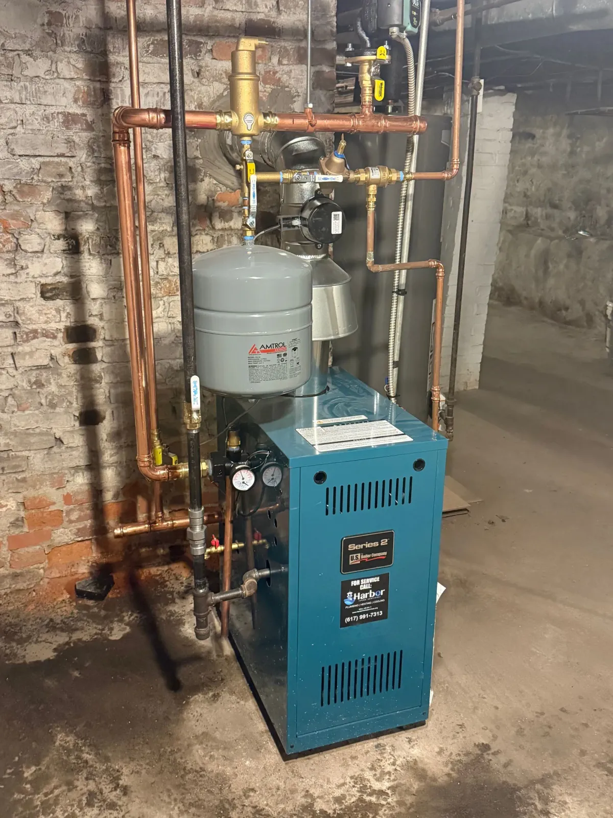 Blue boiler with copper pipes against a brick wall in a basement.