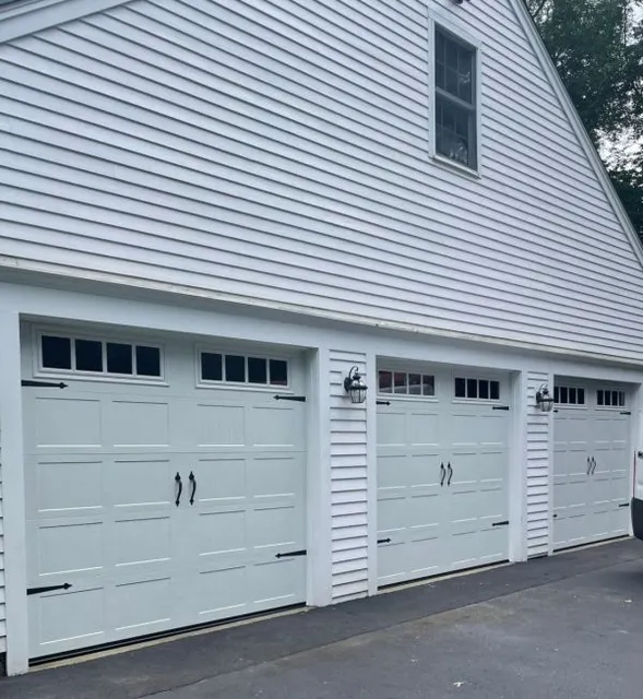 Three white carriage-style garage doors on a white vinyl-sided house exterior