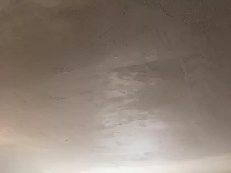A plain white ceiling with visible texture and minor imperfections, including some areas with slight discoloration and irregularities in the plaster.