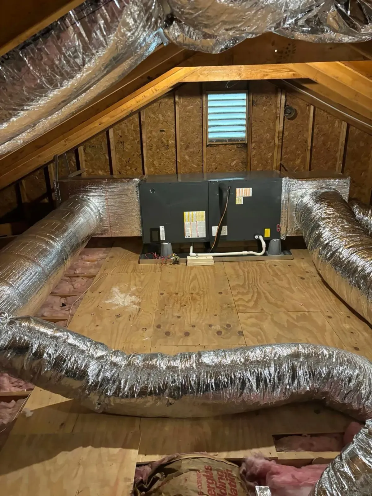 Attic workspace with duct insulation, two monitors, and exposed wood walls and floor