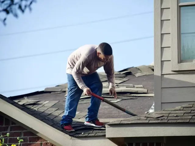 Roofer removing worn shingles from a pitched roof