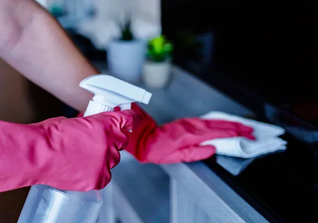 Person wearing pink rubber gloves cleaning a black surface with a spray bottle and a cloth.