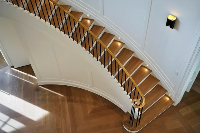 Top view of a curved staircase with wooden steps, black metal railing, and a wooden handrail, inside a home with hardwood flooring and white walls.