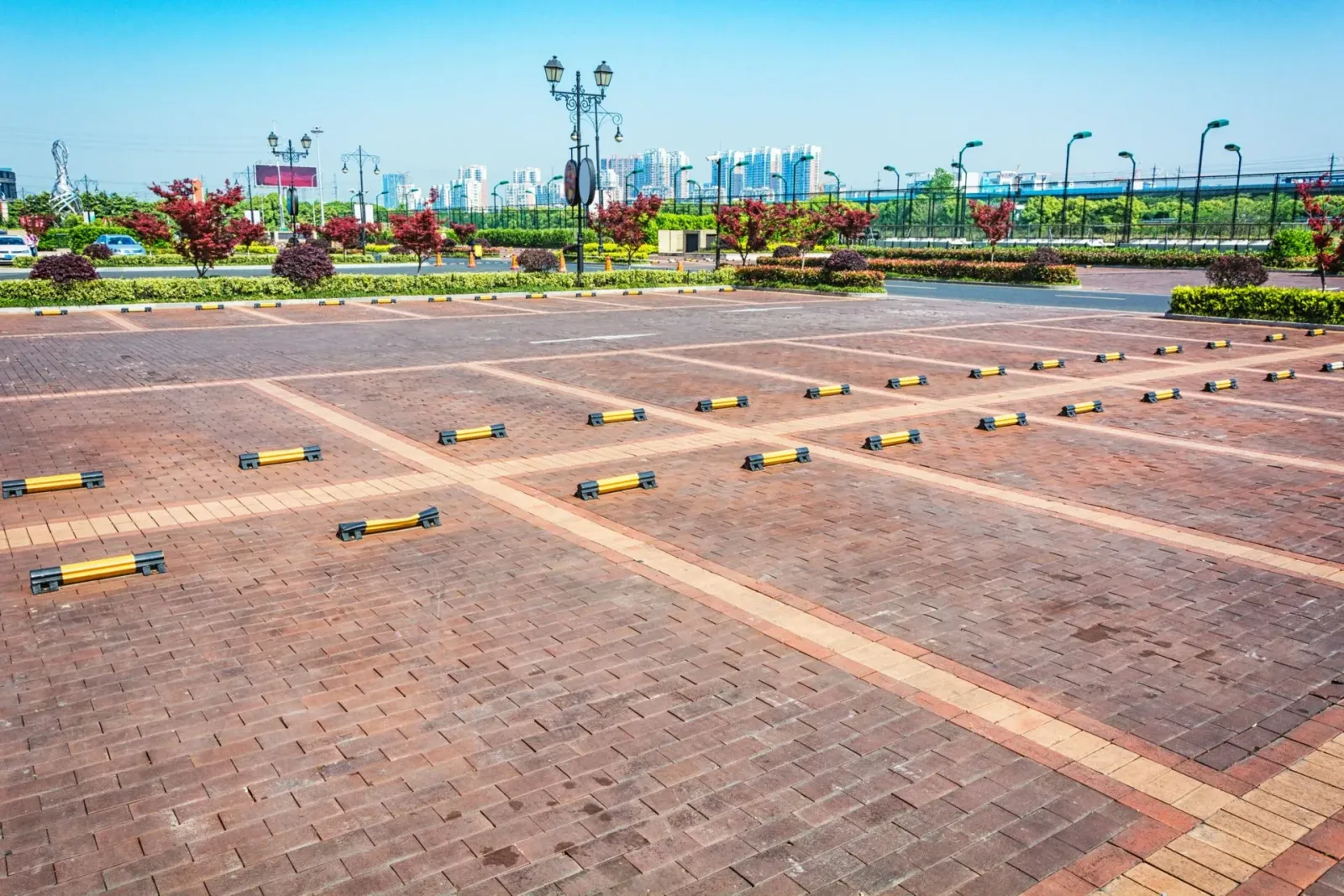 Empty brick-paved parking lot with painted spaces and landscaped greenery in the background