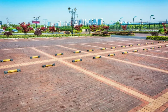 Empty brick-paved parking lot with painted spaces and landscaped greenery in the background