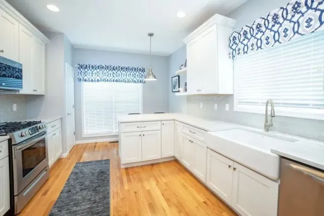 Bright white kitchen with wood floors, stainless appliances, and blue patterned window valances.
