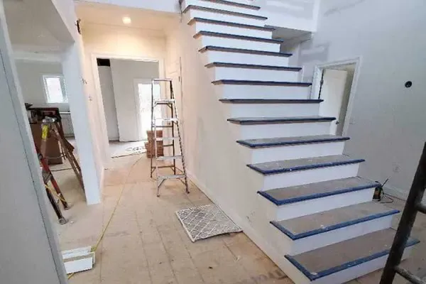 active home construction interior featuring a prominent white staircase with blue-edged treads, ladders, and bare subfloors ready for laminate or LVP flooring installation