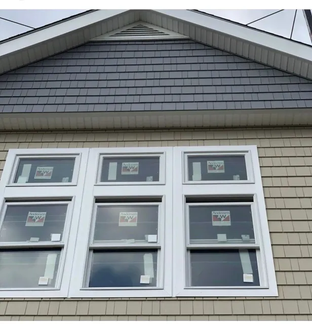 White-framed windows beneath a gray gabled roof on a light beige house exterior