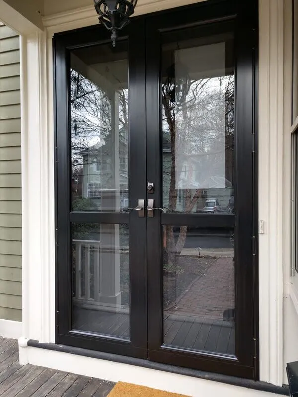 Black-framed French storm doors with full-length glass panels on a covered porch