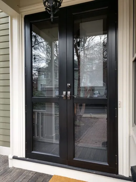 Black-framed French storm doors with full-length glass panels on a covered porch