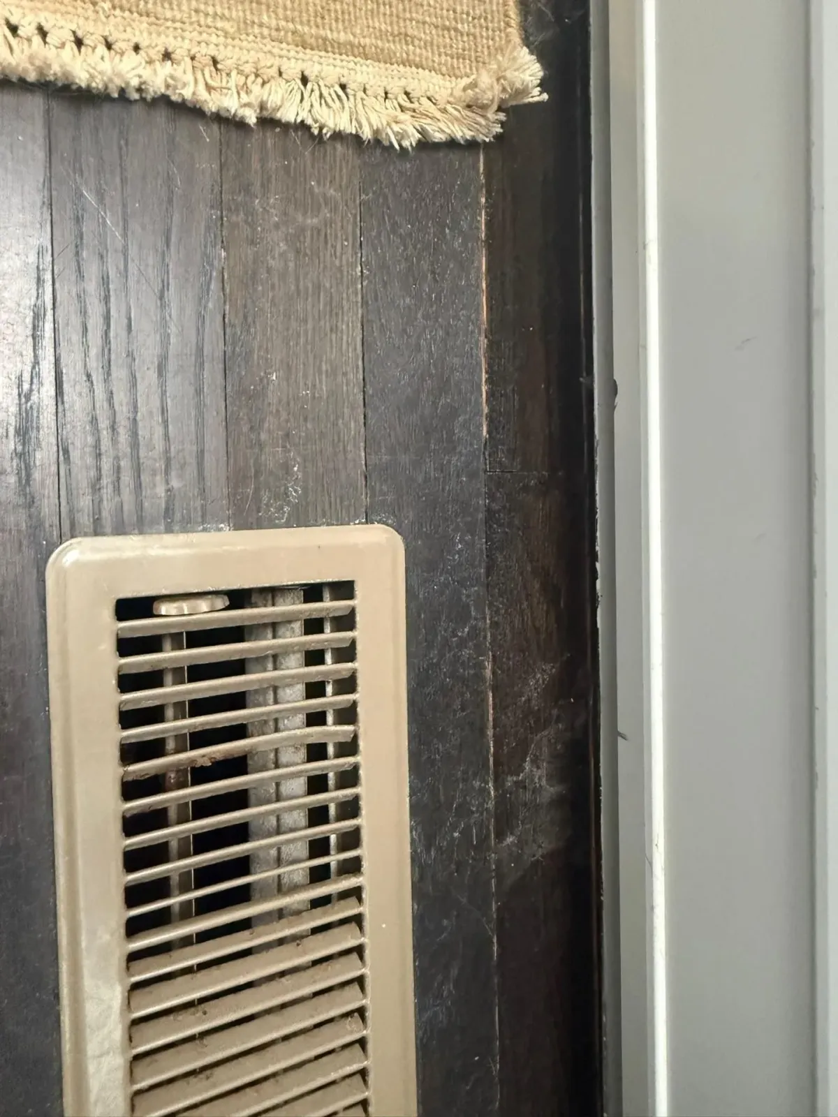 Beige wall vent on dark wood wall beside a light gray surface.