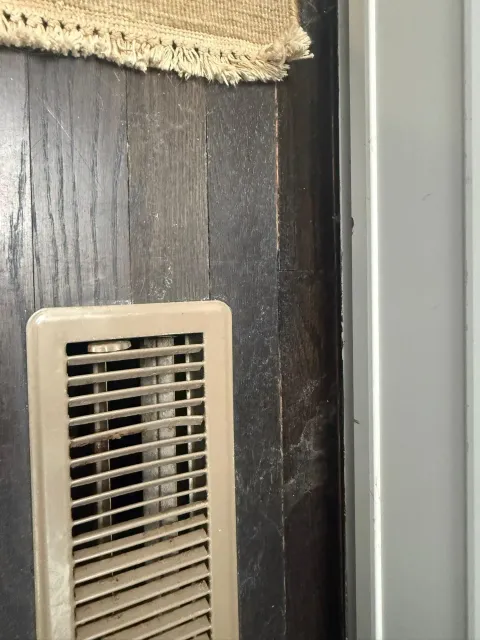 Beige wall vent on dark wood wall beside a light gray surface.