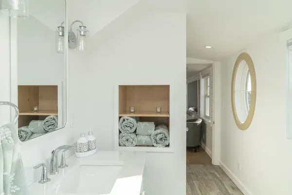 white bathroom with green accents and beige round window by Raymond Design Builders