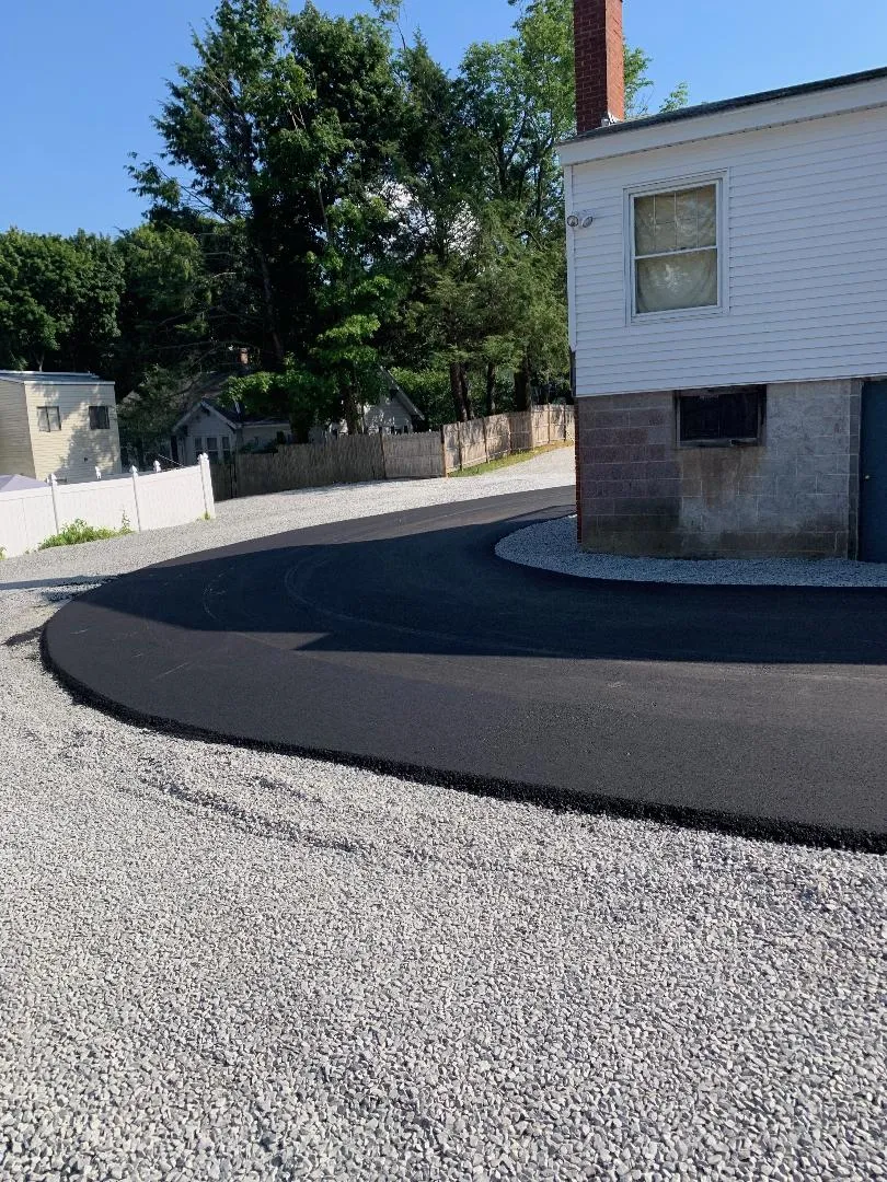 A white house is sitting next to a gravel driveway.