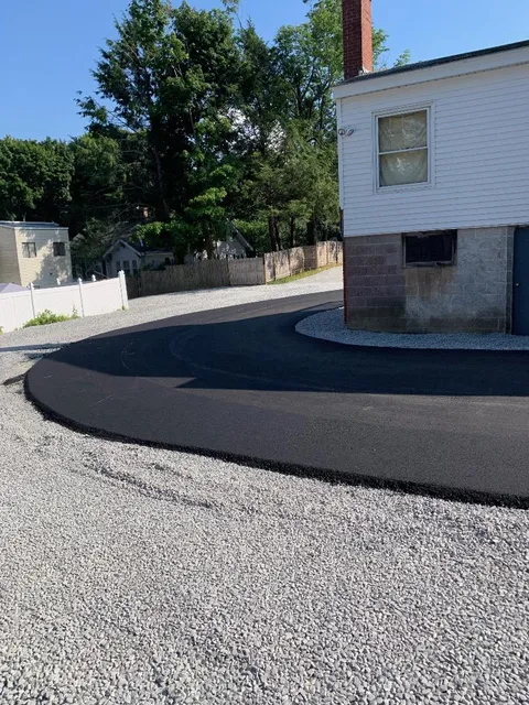 A white house is sitting next to a gravel driveway.