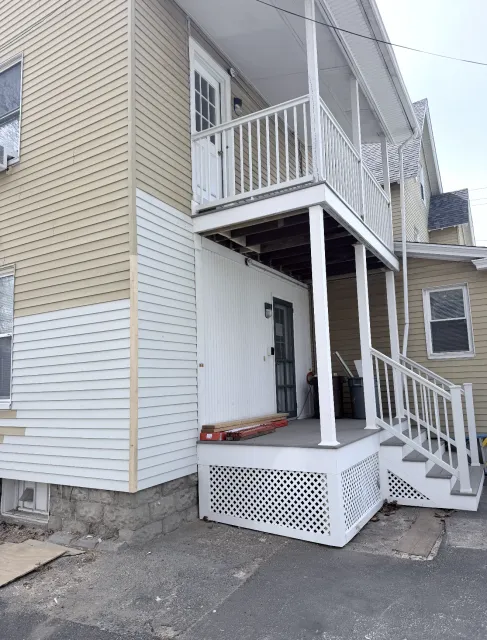 Exterior of a beige house with white balconies, stairs, and a small covered porch.