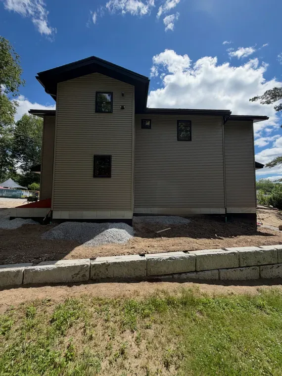 Two-story beige house with dark trim, stone foundation, and a cloudy blue sky overhead