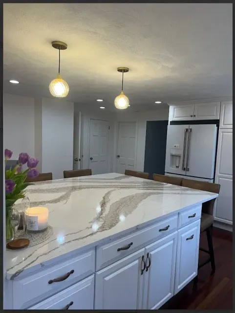 White kitchen island with quartz countertop, pendant lights, cabinets, and seating.
