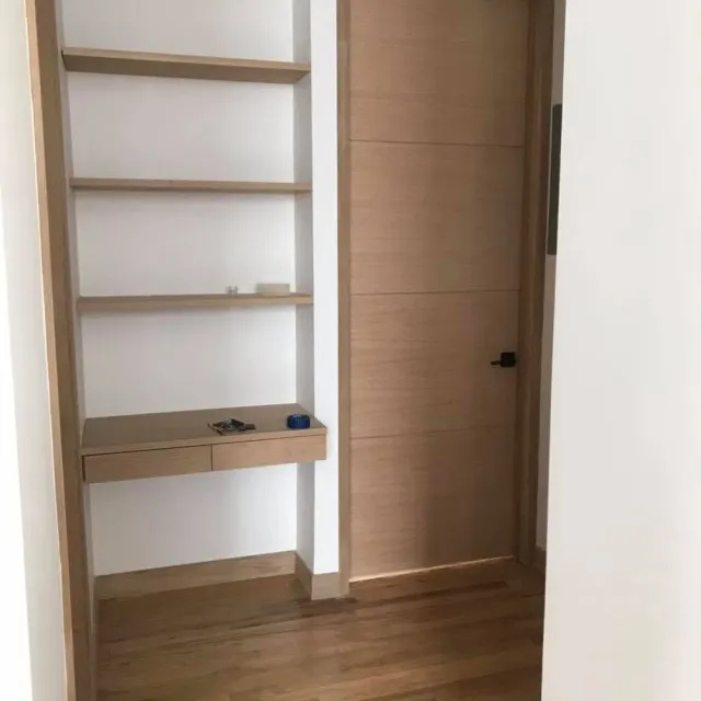 Built-in wooden shelving and a small desk beside a closed wooden door in a minimalist room