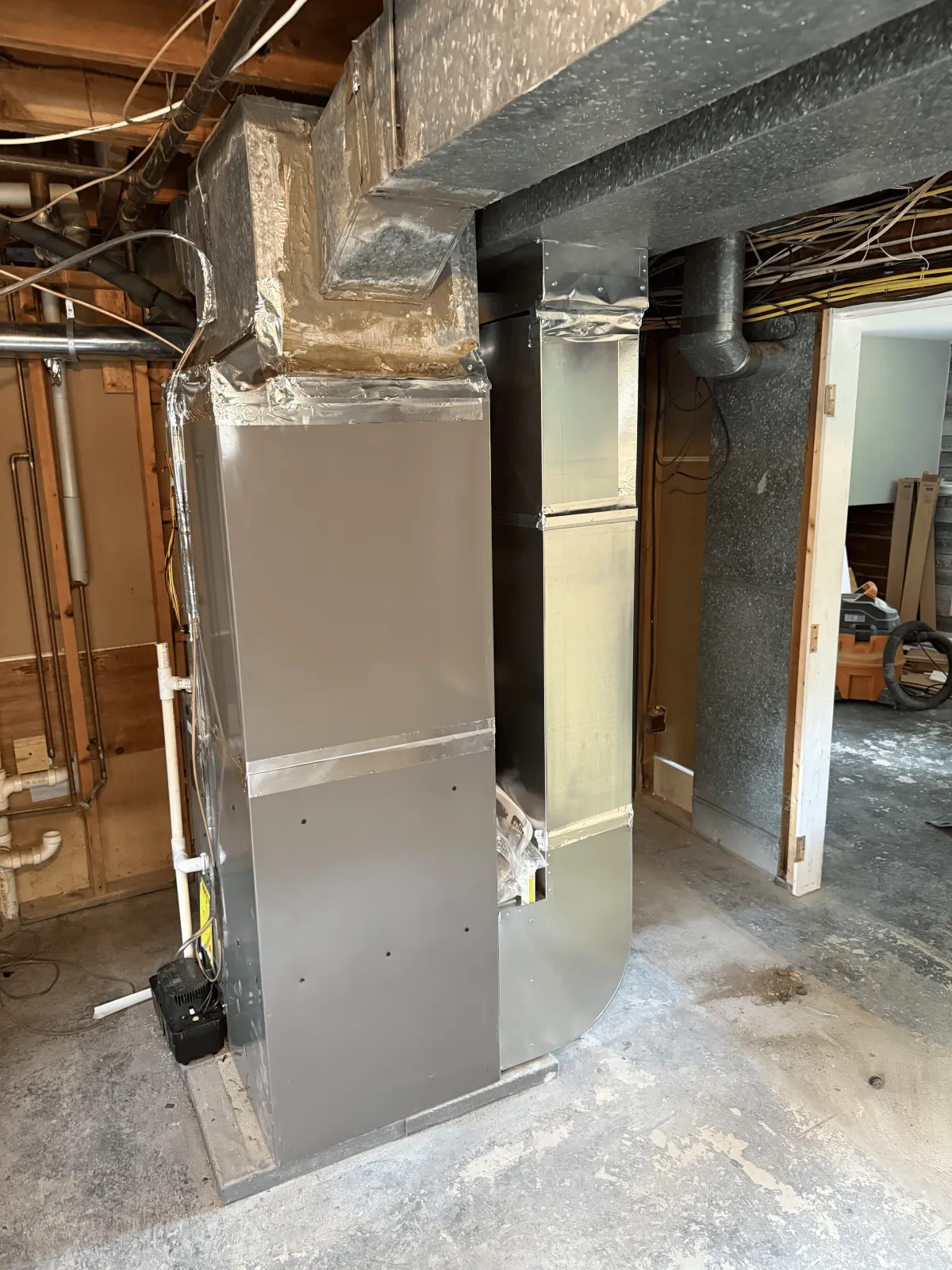 New gray furnace unit installed in basement with black ductwork and foil-sealed connections