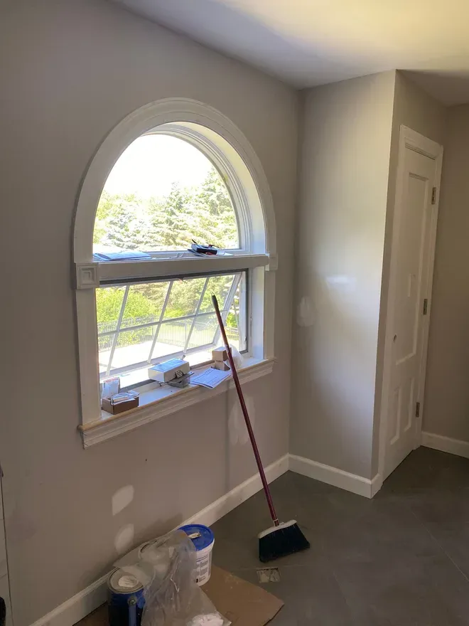 Interior view of a room with an arched window. A closet is to the right. A broom and supplies sit below the window.