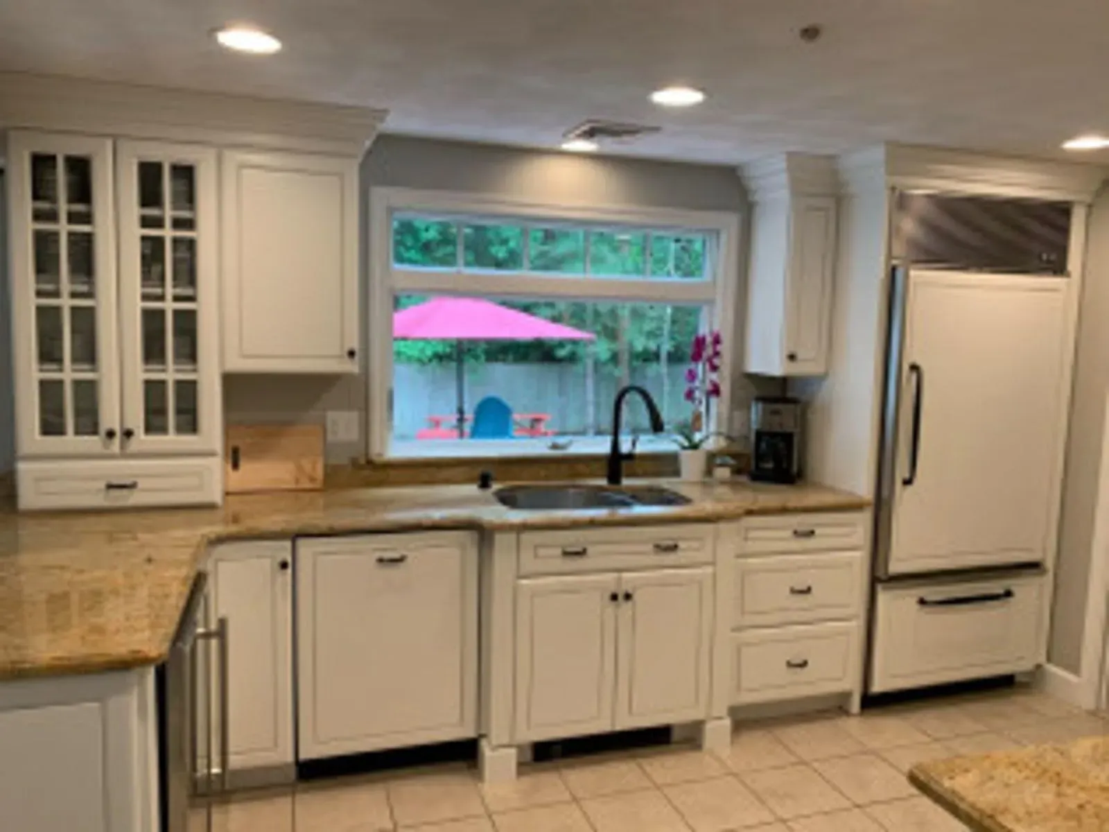 White kitchen with granite countertops, stainless steel appliances, and a window overlooking a backyard.