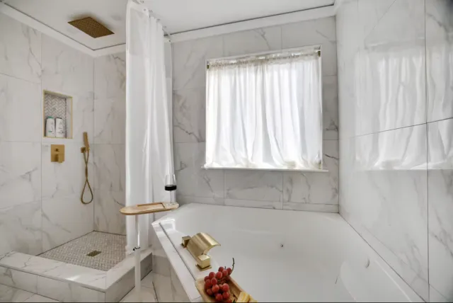 Tub set in marble-look tile with a gold faucet and a window above