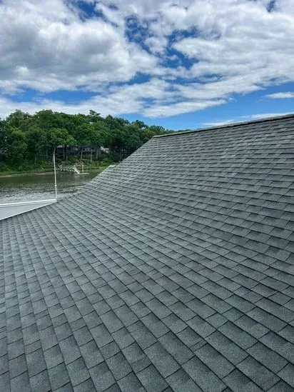 A comprehensive view of the entire gray shingle roofline and the cleaned gutter system, highlighting the proper drainage path established by the residential roof gutter service.