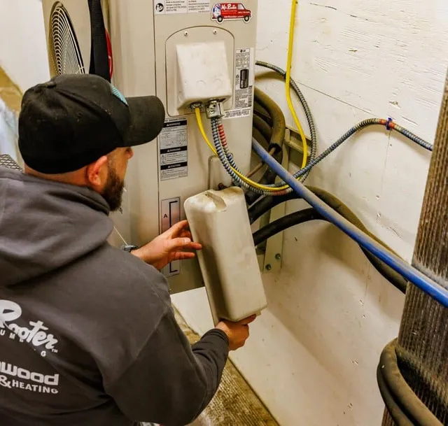 Service technician performing maintenance on heating equipment, showcasing Greenwood Plumbing & Heating branding on uniform, highlighting expertise in HVAC services.