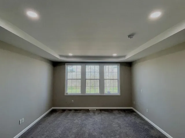 Empty room with beige walls, dark gray carpet, a large window, and recessed ceiling lights.