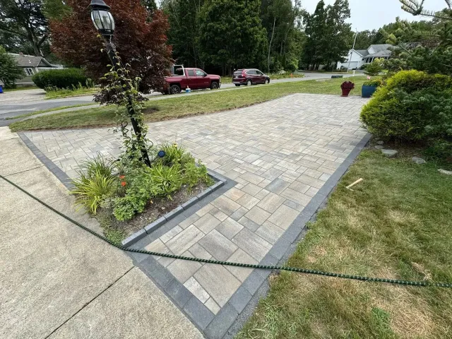 Stone walkway across a landscaped courtyard with trees, shrubs, and parked cars nearby.
