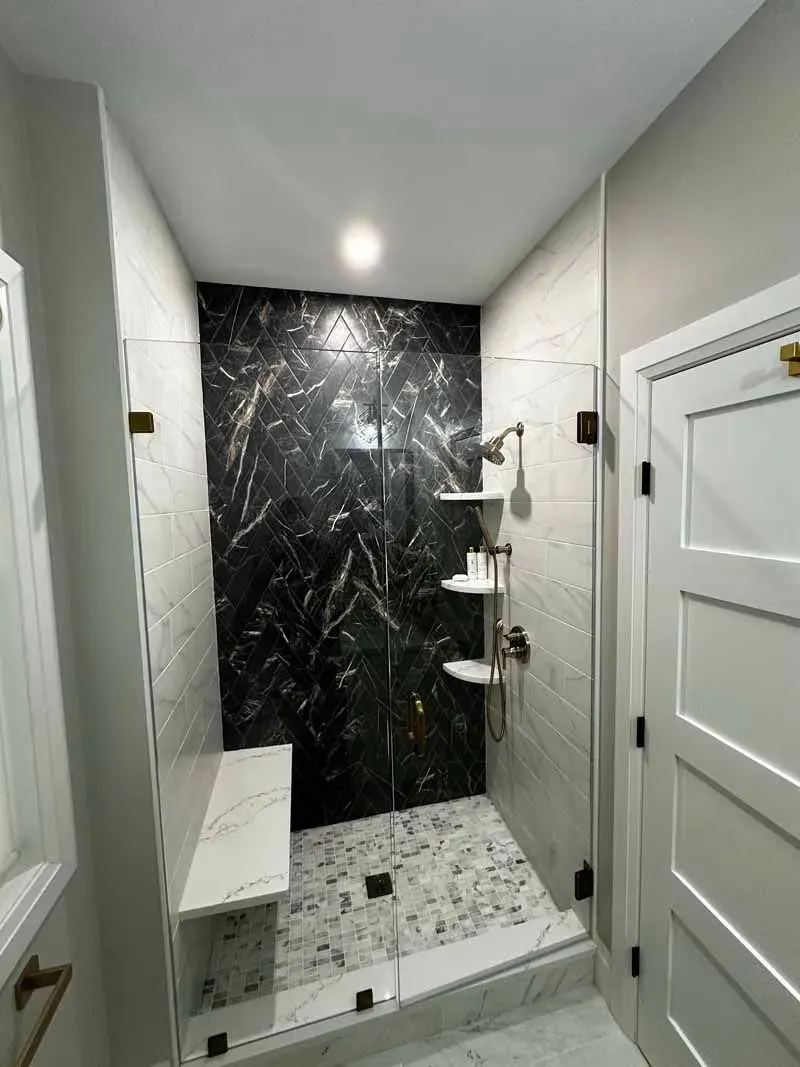 Modern shower with marble and black stone accent wall, bench, and shelves.