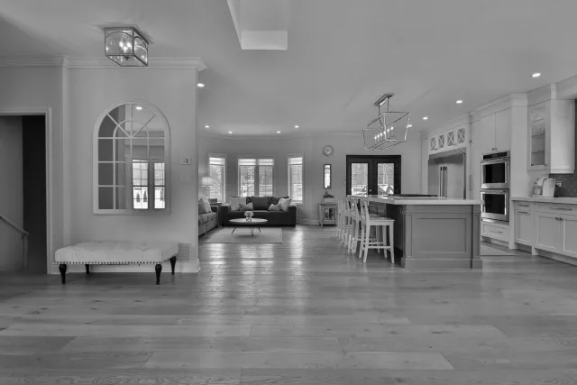 Open-concept living room and kitchen with large windows, hardwood floors, pendant lighting, and modern cabinetry.