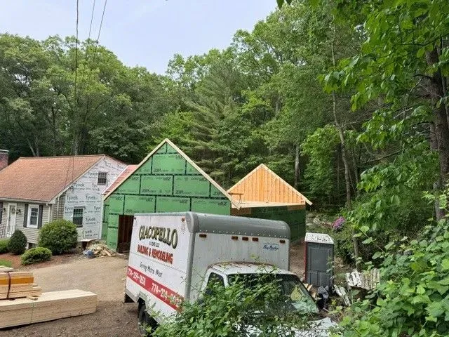 White house and green-roofed buildings beside a moving truck in a wooded driveway