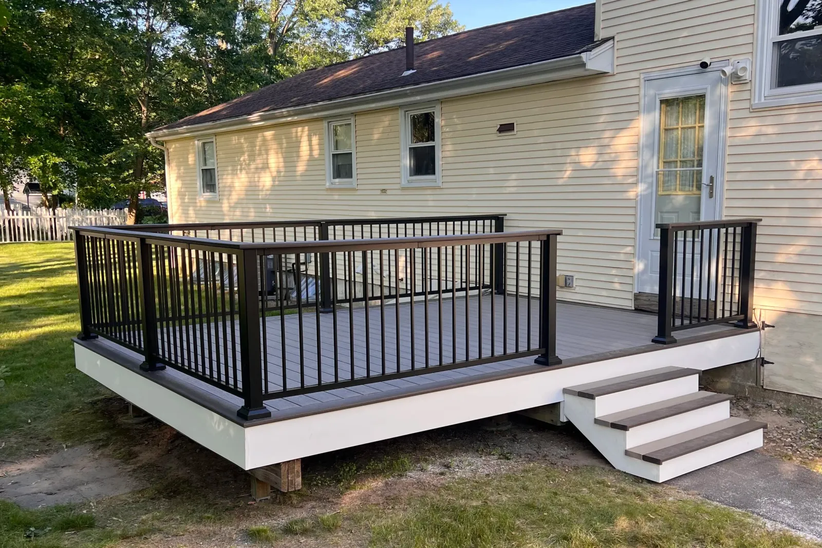 Newly built outdoor wooden deck with black metal railing , accessed by white stairs with dark wood treads.