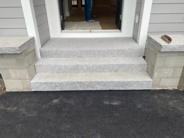 Exterior gray speckled steps leading to a doorway. Concrete pillars on either side.