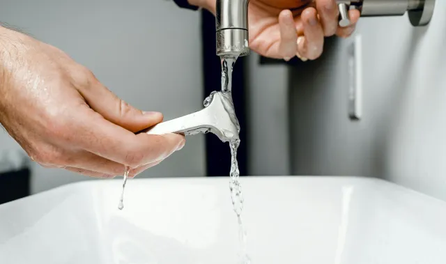 Person turning on a kitchen faucet with water flowing into a white sink.